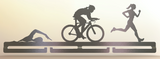 A metal medal hanger with a combination of silhouettes of a swimmer, a cyclist, and a runner, mounted on a wall.