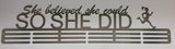 A brushed stainless steel decorative plaque with the inscription 'She believed she could SO SHE DID' accompanied by a silhouette of a runner, mounted on a wall.